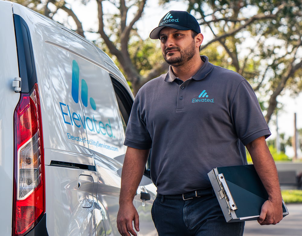 An elevator technician standing next to a service van with the company logo, holding a clipboard.