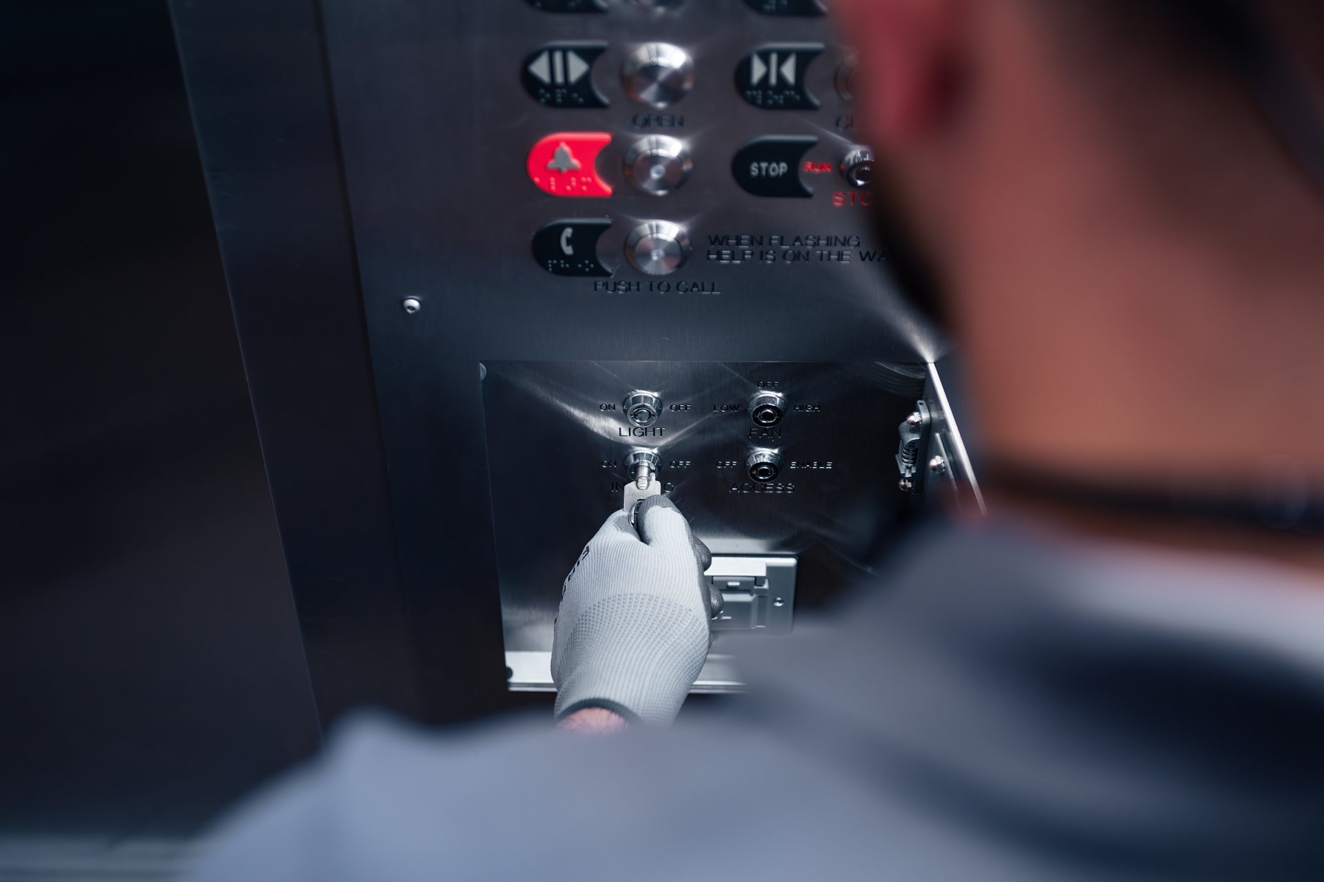 Close-up of an elevator technician's hand using a tool on a control switch in the elevator's control panel.