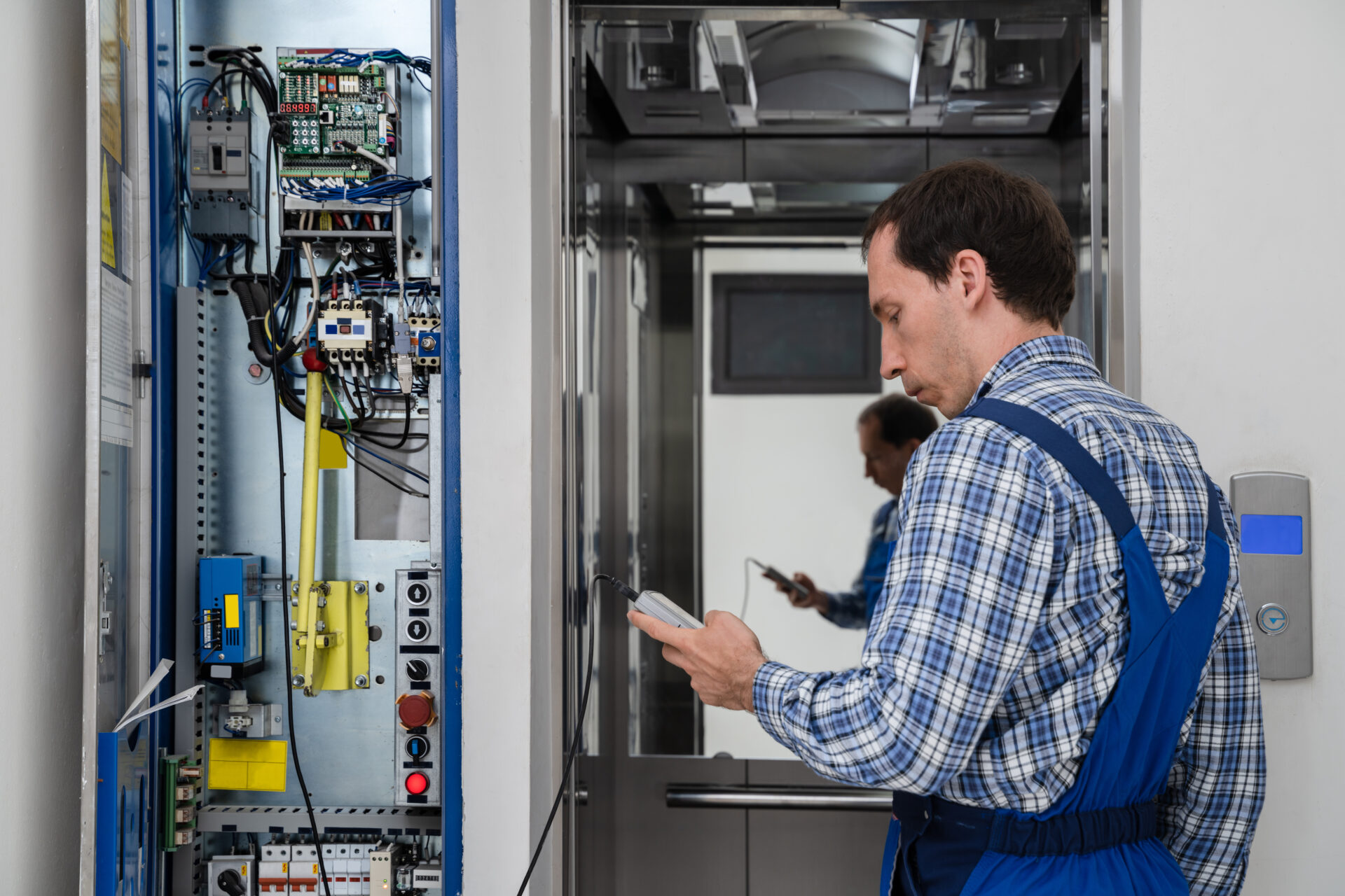 Elevator technician working beside an open control panel and elevator car.