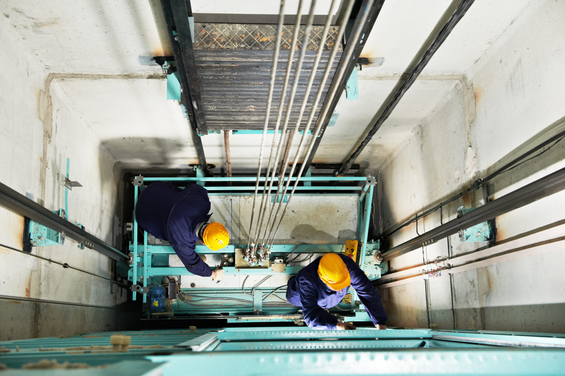 Overhead view of two technicians working inside an elevator shaft.